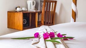 A neatly made bed with a white sheet and a decorative arrangement of pink flowers and green leaves. - Anna & Gideon's  B&B (Jambiani)