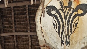 A rustic thatched roof structure with a wooden post and a white wall with a black design. - Anna & Gideon's  B&B (Jambiani)