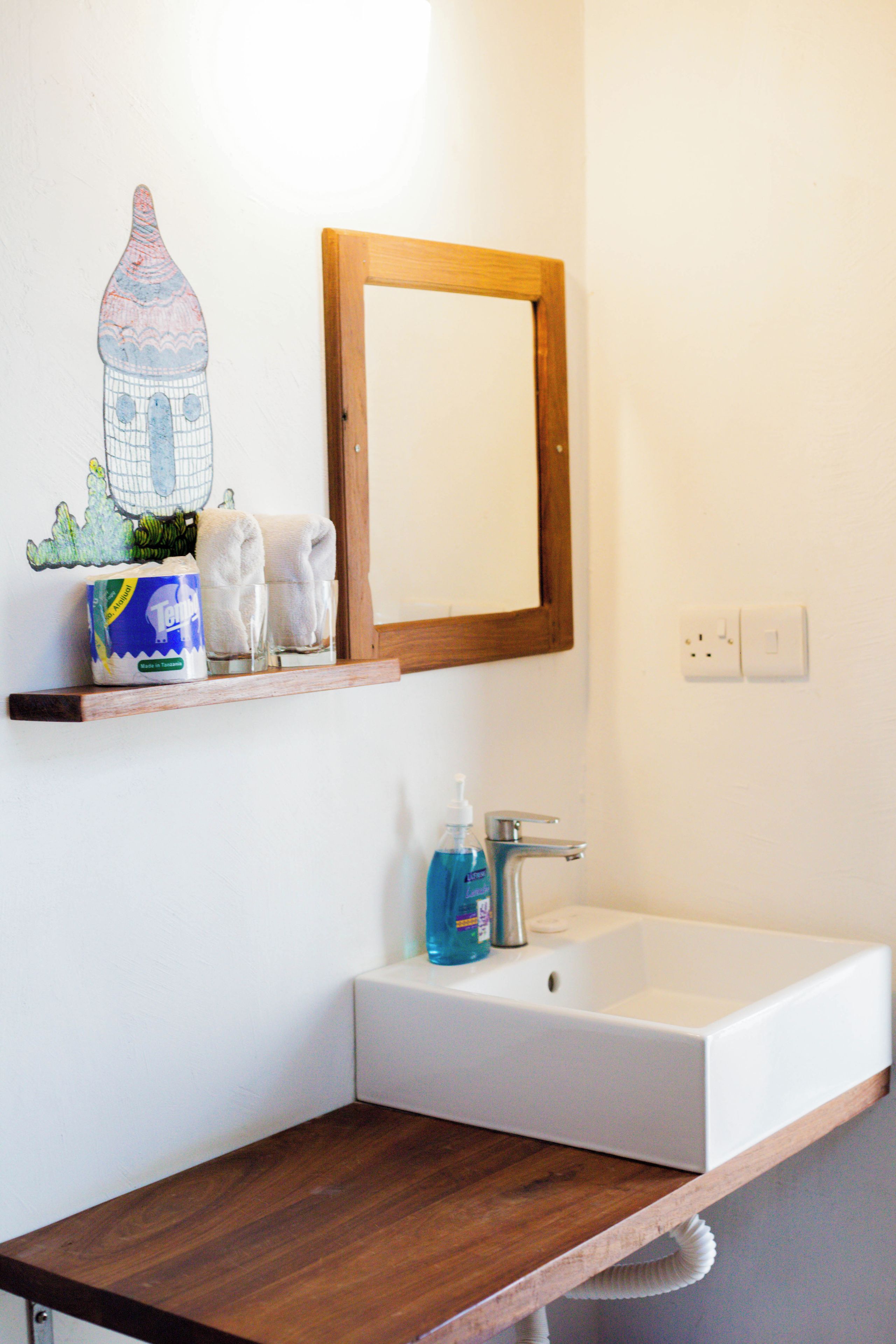Een badkamer met een witte wastafel, een houten plankje met toiletartikelen en een spiegel.