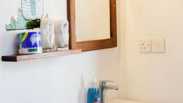 Een badkamer met een witte wastafel, een houten plankje met toiletartikelen en een spiegel.
