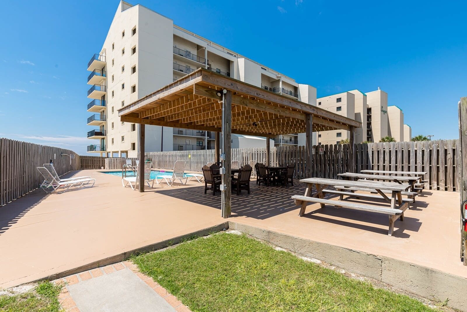 A covered outdoor area with a pool, lounge chairs, and picnic tables.