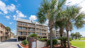A multi-story hotel with balconies, palm trees, and a well-maintained lawn.