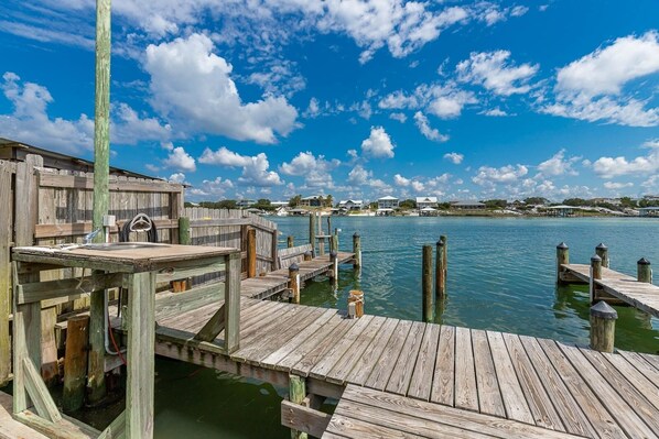 A wooden dock extending into calm water, with a clear sky and distant buildings.