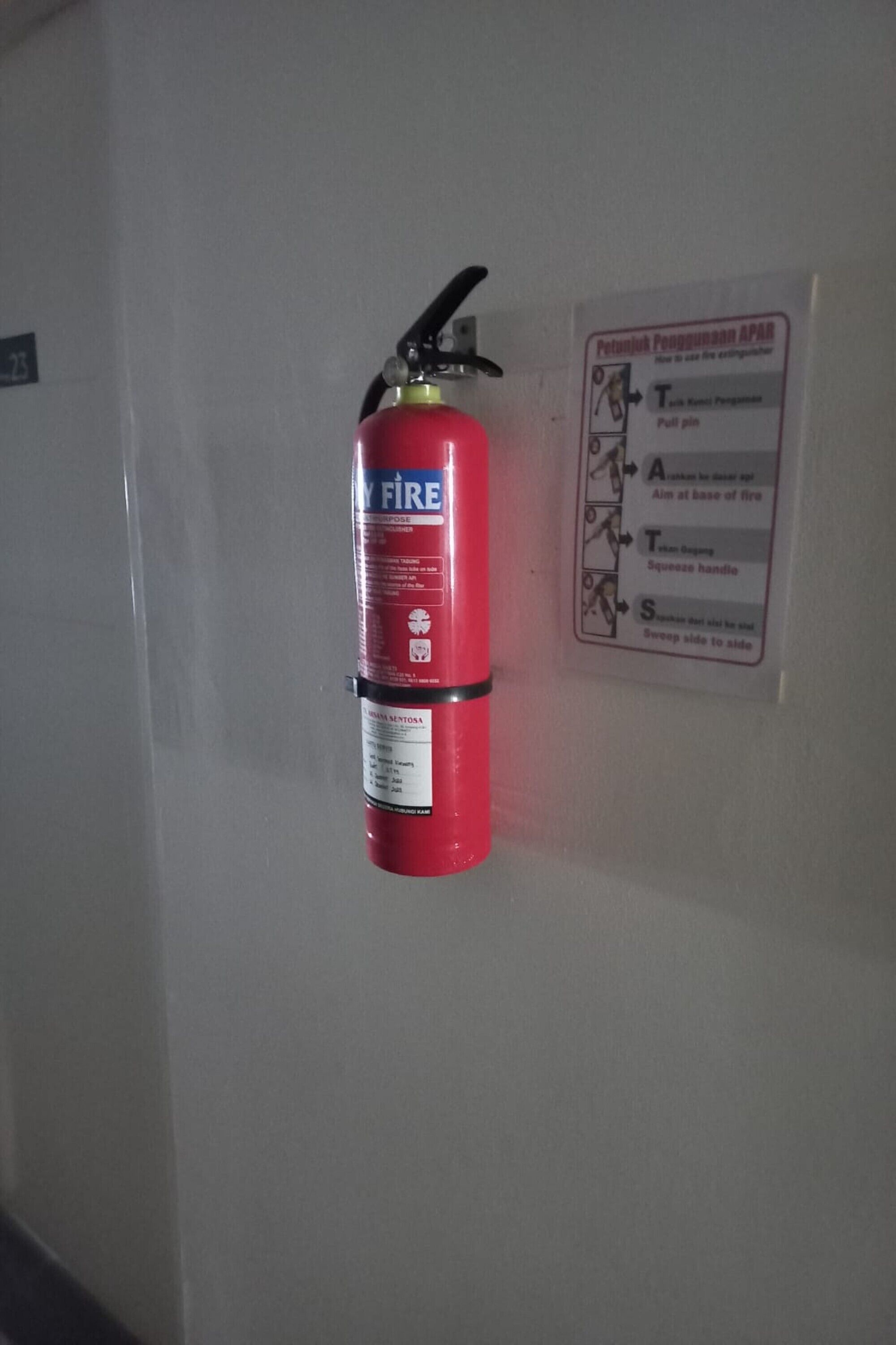 A red fire extinguisher mounted on a wall next to a safety instruction sign.