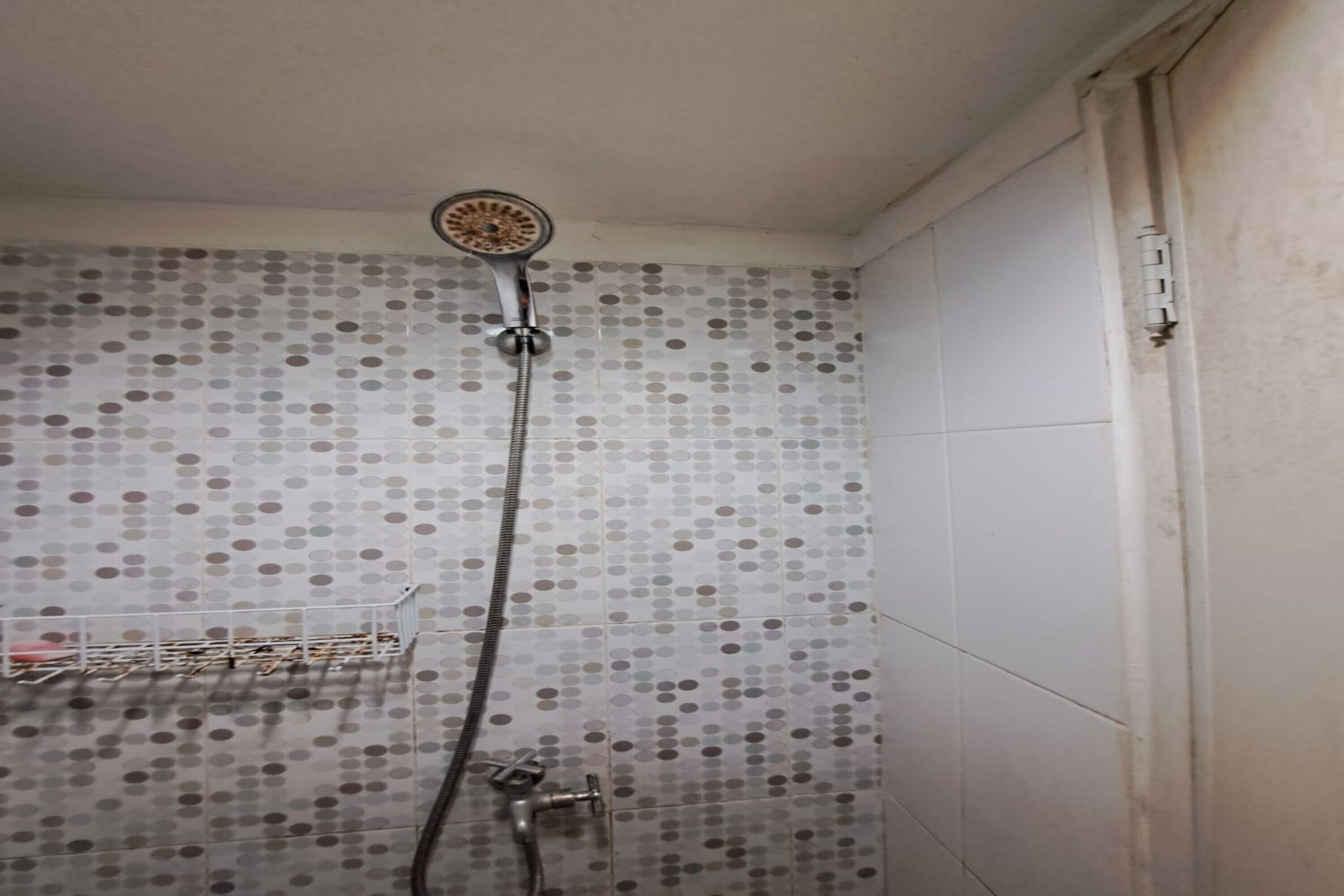 A shower with a handheld showerhead, a wall-mounted faucet, and a tiled wall with a polka dot pattern.
