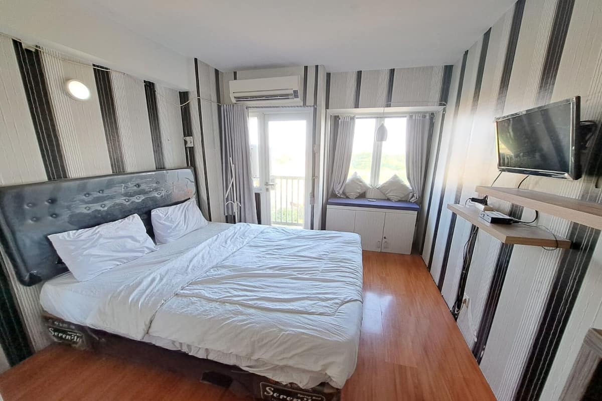 A bedroom with a bed, an air conditioning unit, a television, and a window with curtains.