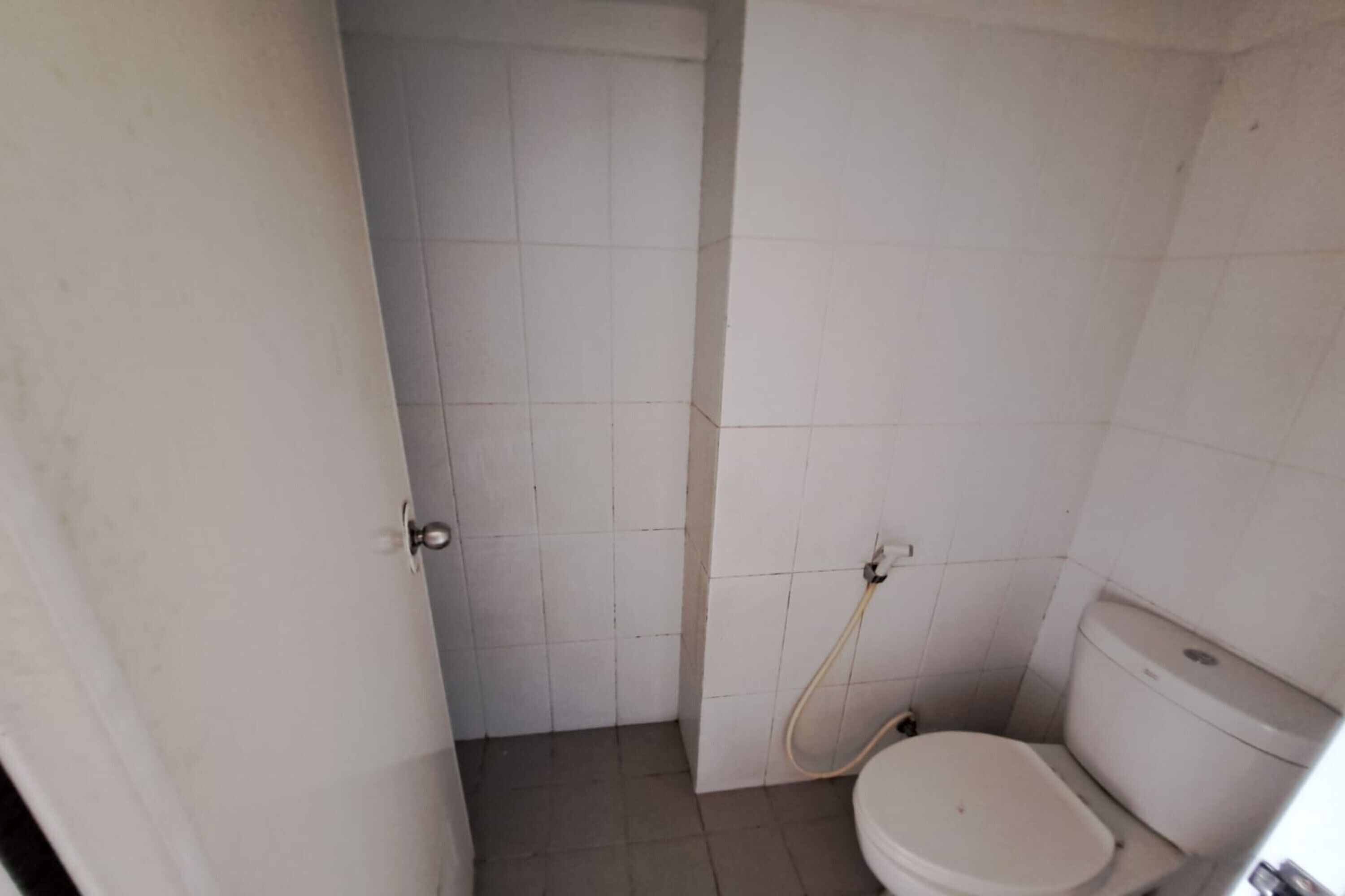Une petite salle de bain carrelée, équipée de toilettes et d’une zone douche.