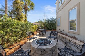 Eine Terrasse mit Sitzgelegenheiten im Freien, einer Feuerstelle und umgebender Bepflanzung.