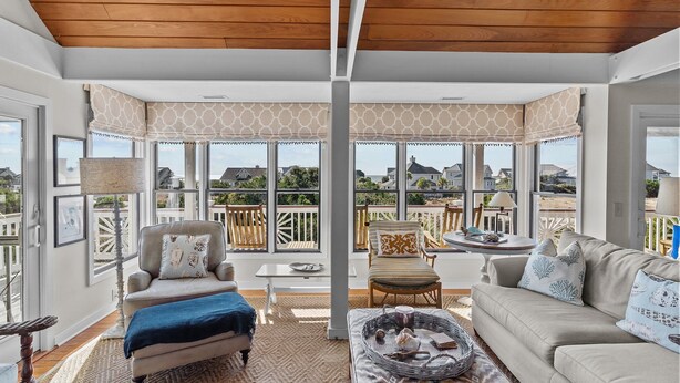 A spacious room with a high ceiling, large windows, and a view of the outdoors. There are two sofas, a coffee table, and a small table with chairs.