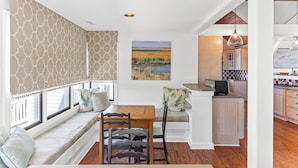 A cozy dining area with a bench, a wooden table, and chairs. There is a kitchen visible in the background with a checkered backsplash.