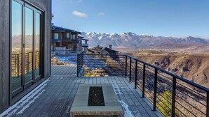Eine Holzterrasse mit einer Steinsitzbank, einem Metallgeländer und Blick auf schneebedeckte Berge.