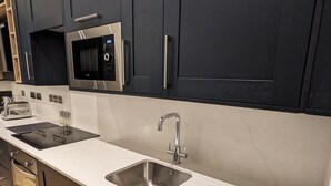 Une cuisine moderne avec des meubles de couleur sombre, des appareils en acier inoxydable et un plan de travail blanc.
