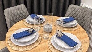 Une table de salle à manger ronde, mise avec des assiettes, des couverts et des verres, entourée de chaises à revêtement gris.