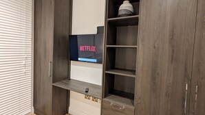 Un meuble-penderie moderne doté d’un téléviseur intégré affichant le logo de Netflix, une télécommande posée sur l’étagère inférieure et un objet décoratif sur l’étagère supérieure.