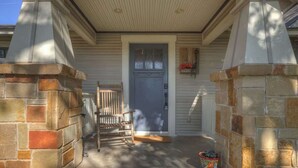 A porch with a wooden rocking chair, a gray door, and a flower box.