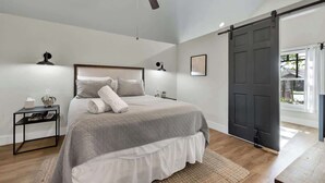 A bedroom with a bed, bedside tables, a ceiling fan, a sliding door, and a view of the outdoors.