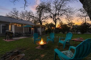 A backyard with a fire pit, outdoor seating, and a house with a covered patio.