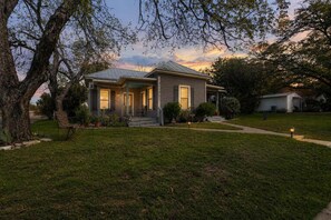 A residential house with a porch, a lawn, and a tree in the foreground.