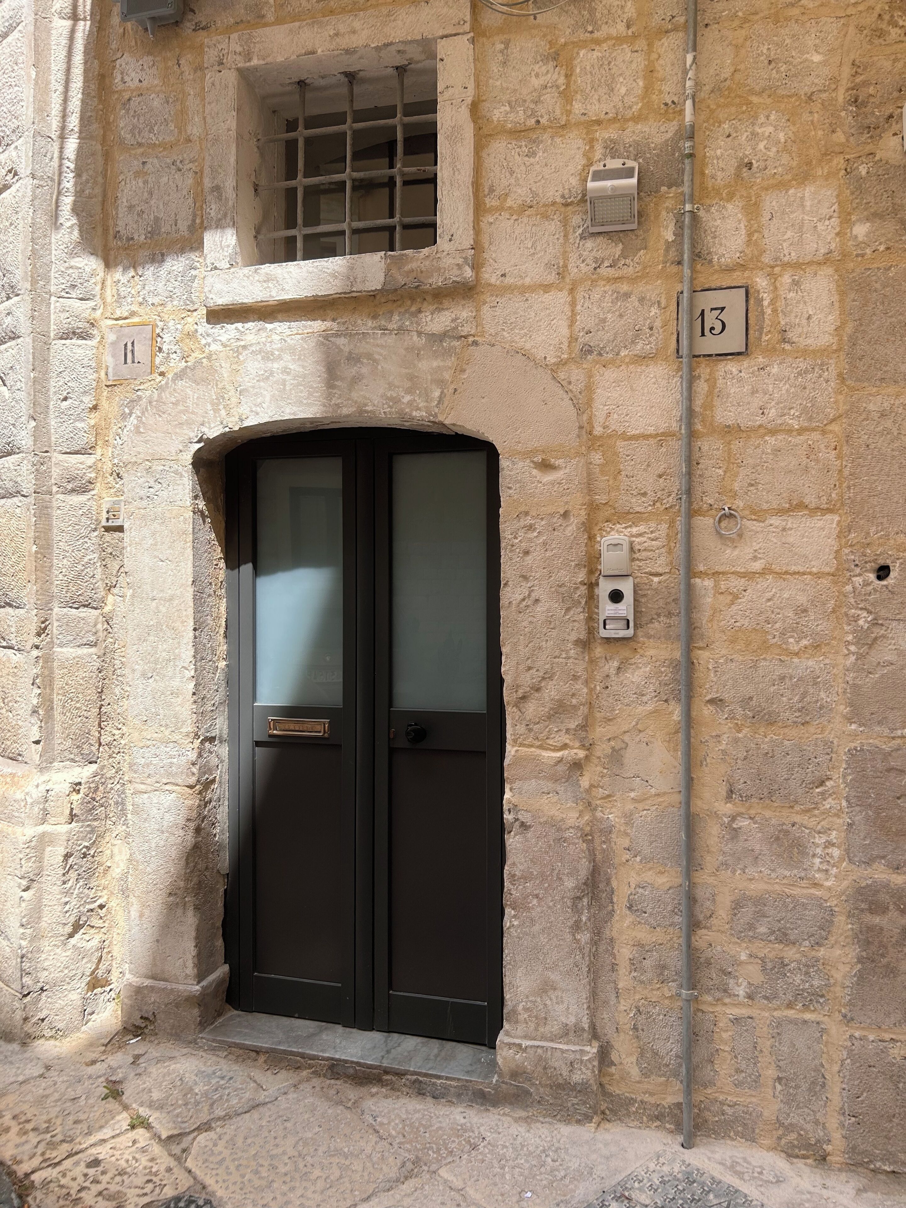 A stone building with a black door, a window with bars, and a number plate '13'.