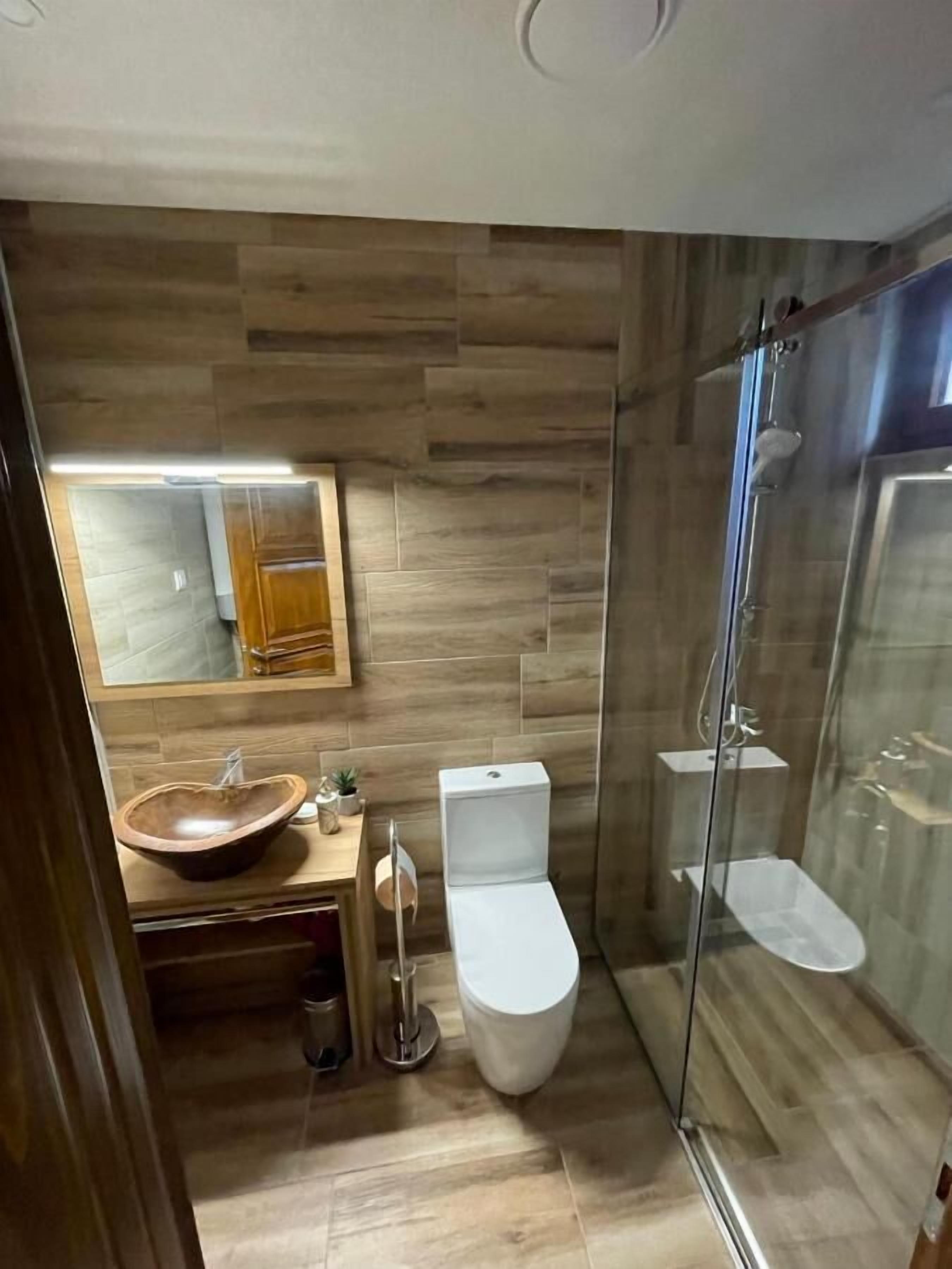 Un bagno moderno con una parete in legno, una cabina doccia in vetro e un water bianco.