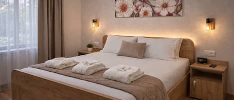 A hotel room with a large bed, two bedside tables, a nightstand, a wall-mounted painting, and a window with curtains.