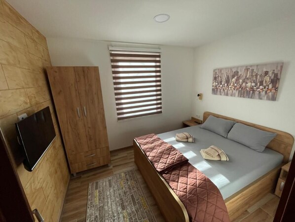 A bedroom with a bed, a TV mounted on the wall, a window with blinds, and a painting on the wall. - Casa Mia Vrdnik (Vrdnik)