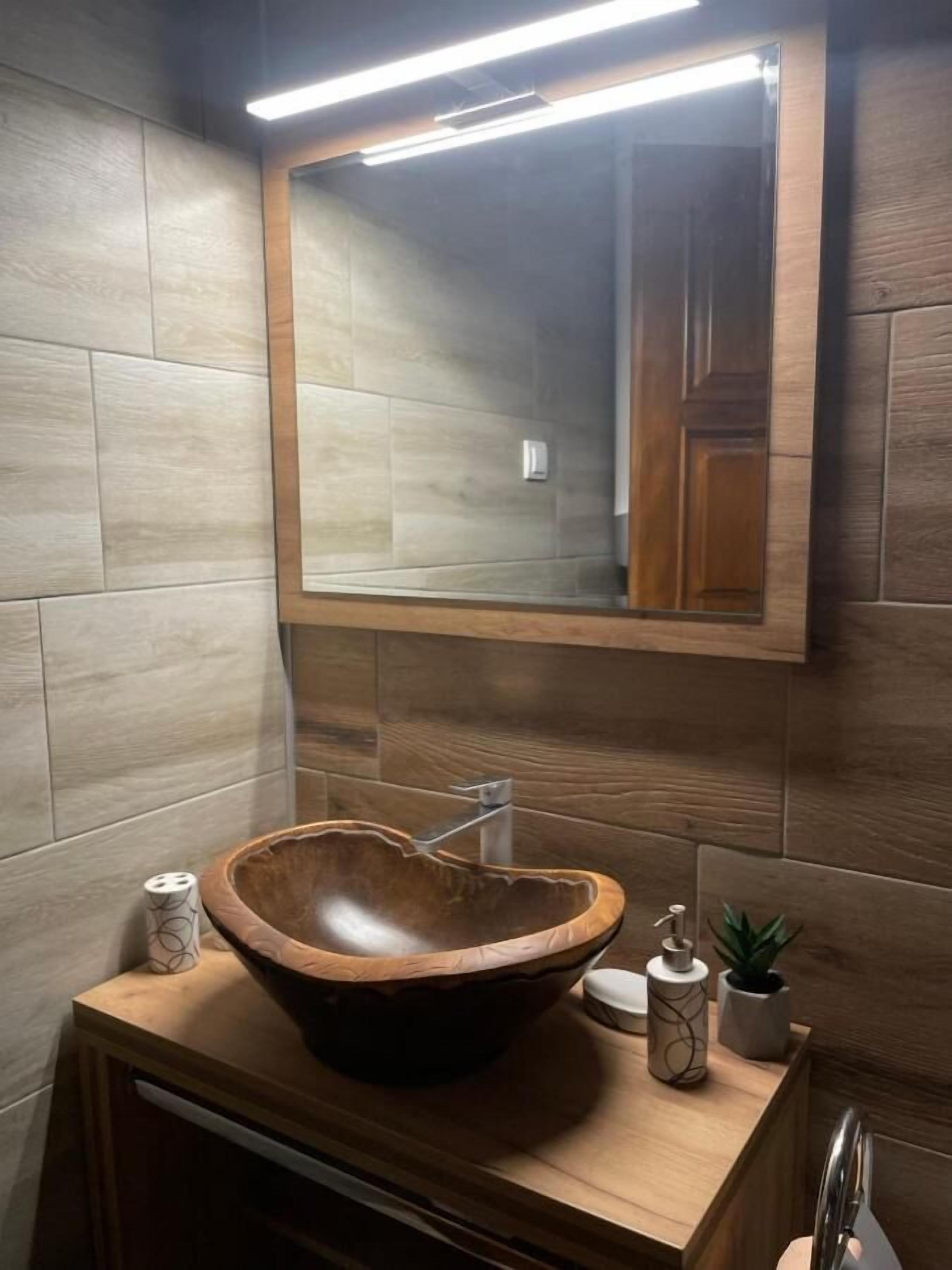 Een badkamer met een houten wastafelmeubel, een grote spiegel en een waskom.