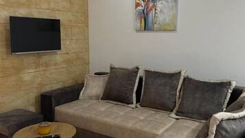 Ein modernes Wohnzimmer mit einer Eckcouch, einem flachbildfernseher an einer Steinwand und einem Gemälde über der Couch.