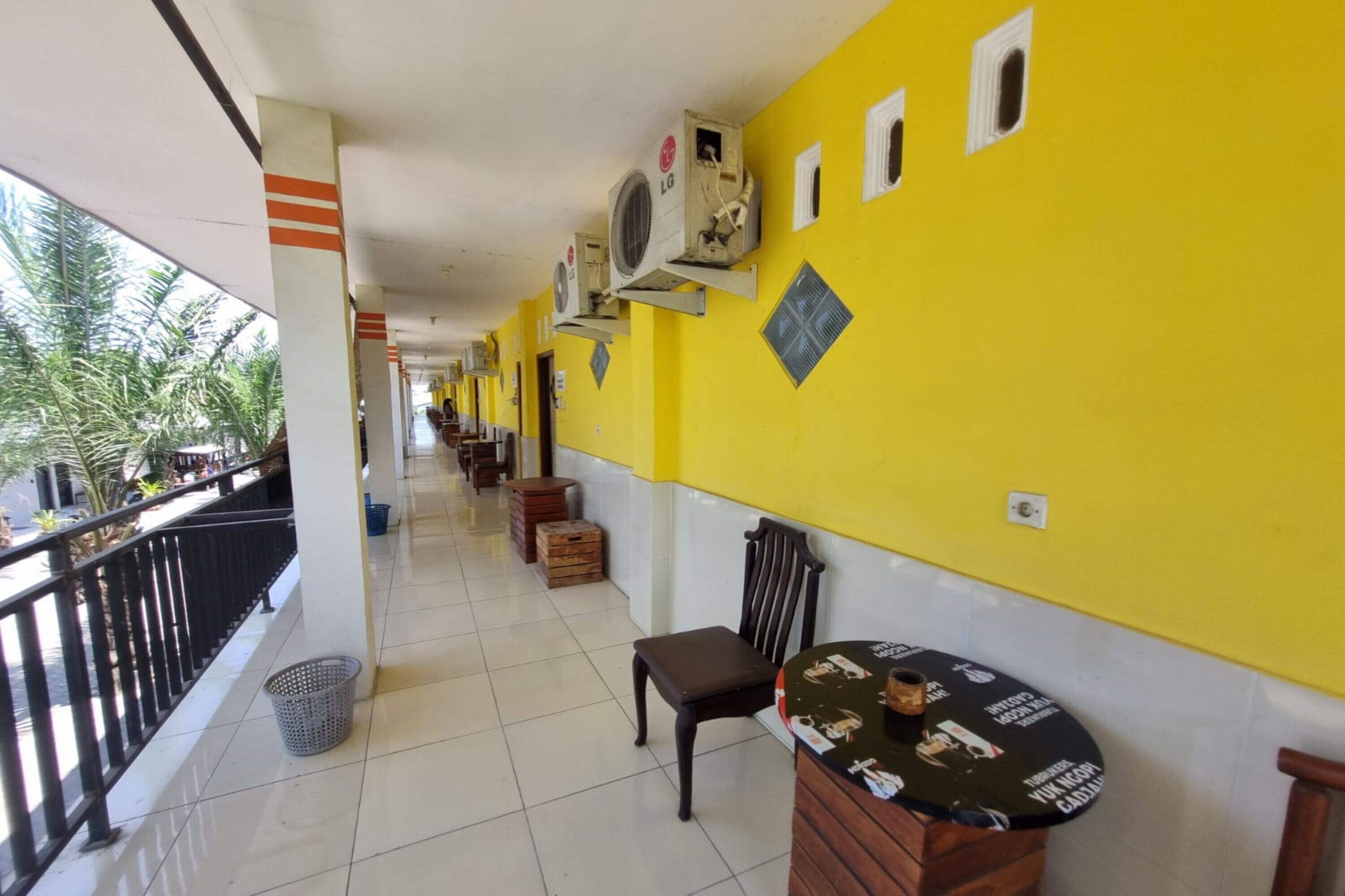 A corridor with yellow walls, air conditioning units, a trash bin, and a table with a placemat.