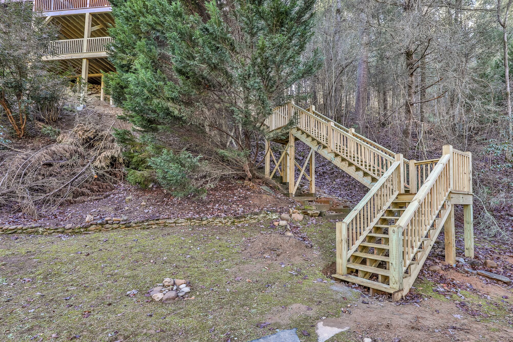 A wooden staircase leading up to a wooden deck, surrounded by trees and a small stream.