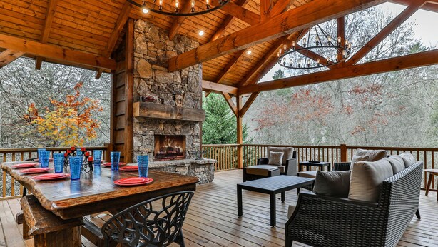 A wooden deck with a stone fireplace, outdoor seating, and a dining area with blue glasses and red plates.