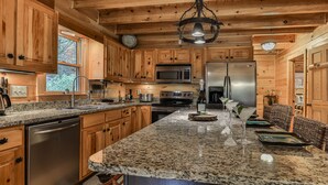 A kitchen with wooden cabinets, granite countertops, stainless steel appliances, and a hanging light fixture.