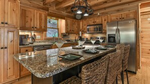 A kitchen with wooden cabinets, granite countertops, a stainless steel refrigerator, and a hanging light fixture.