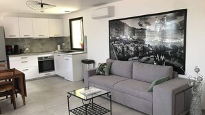 Een moderne woonkamer met een grijze bank, een glazen salontafel, en een eethoek met een houten tafel en stoelen. Een groot zwart-wit stadsgezichtsiers de muur.