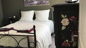 Een slaapkamer met een bed, een nachtkastje, een dressoir met bloemkunst en een aan de muur hangend schilderij.
