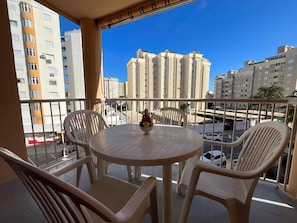 Een balkon met een ronde tafel en vier stoelen, met uitzicht op een stadsgezicht met hoge gebouwen.