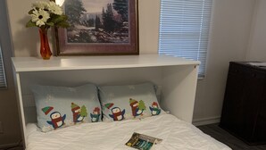 Un dormitorio con una cama blanca, una colcha rosa, un cuadro enmarcado de un paisaje y almohadas con motivos nevados.