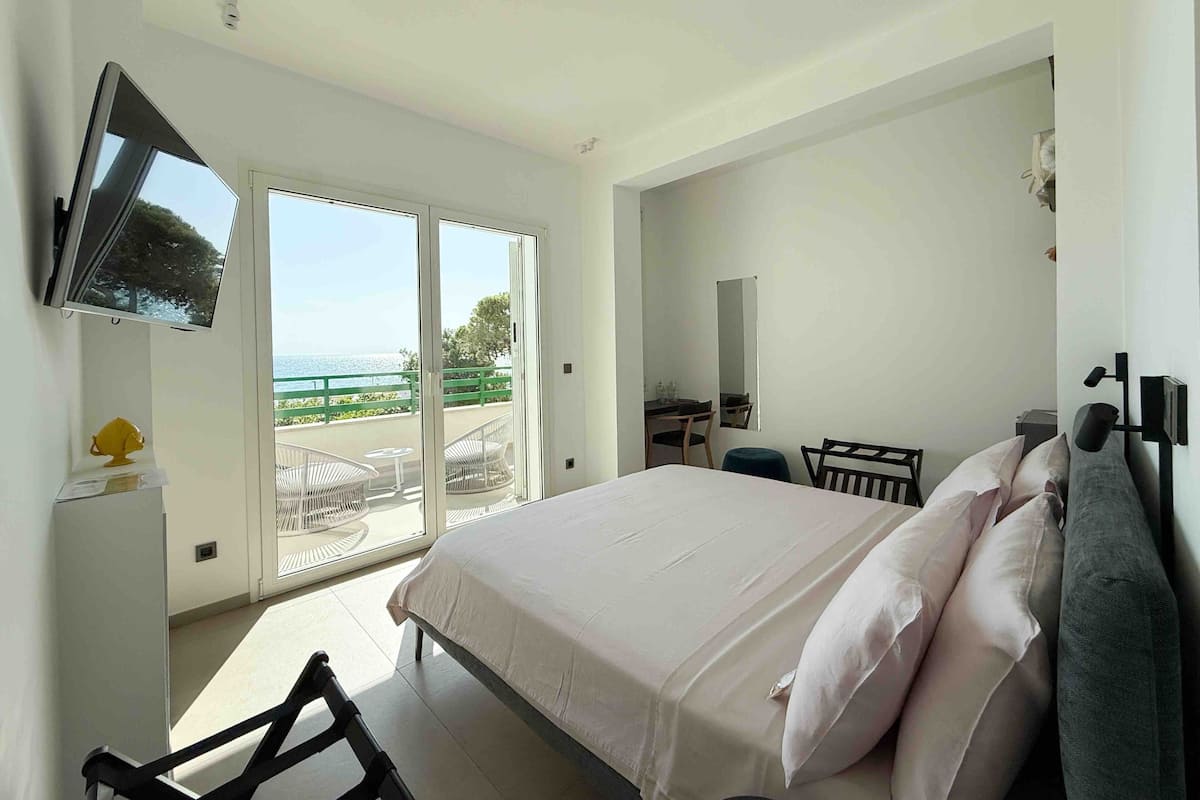 Une chambre à coucher avec un lit, un téléviseur fixé au mur, un bureau avec une chaise et un balcon donnant sur la mer.