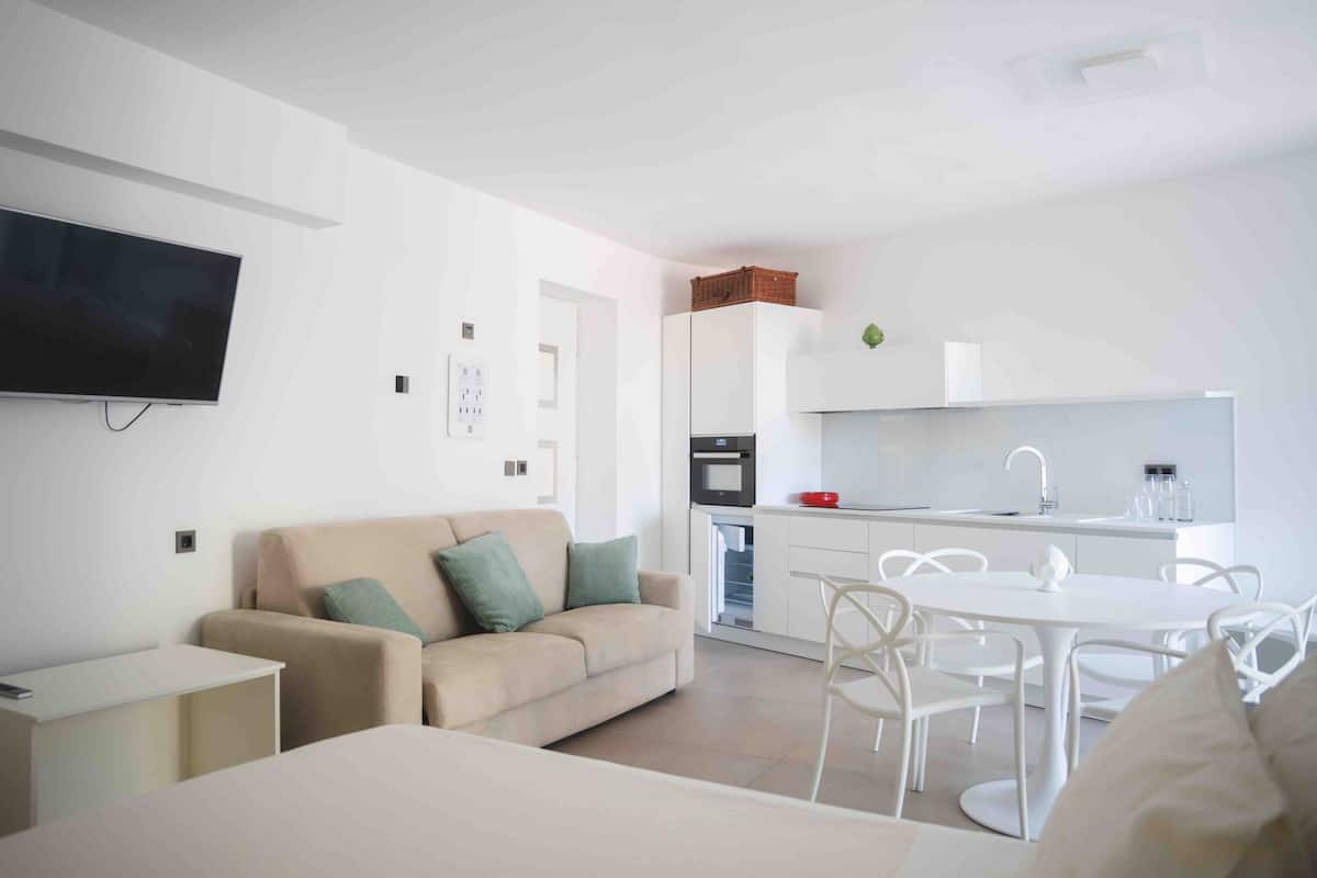 Un salon moderne comprenant un canapé, un téléviseur, une table à manger avec des chaises et un coin cuisine avec un réfrigérateur et un four à micro-ondes.