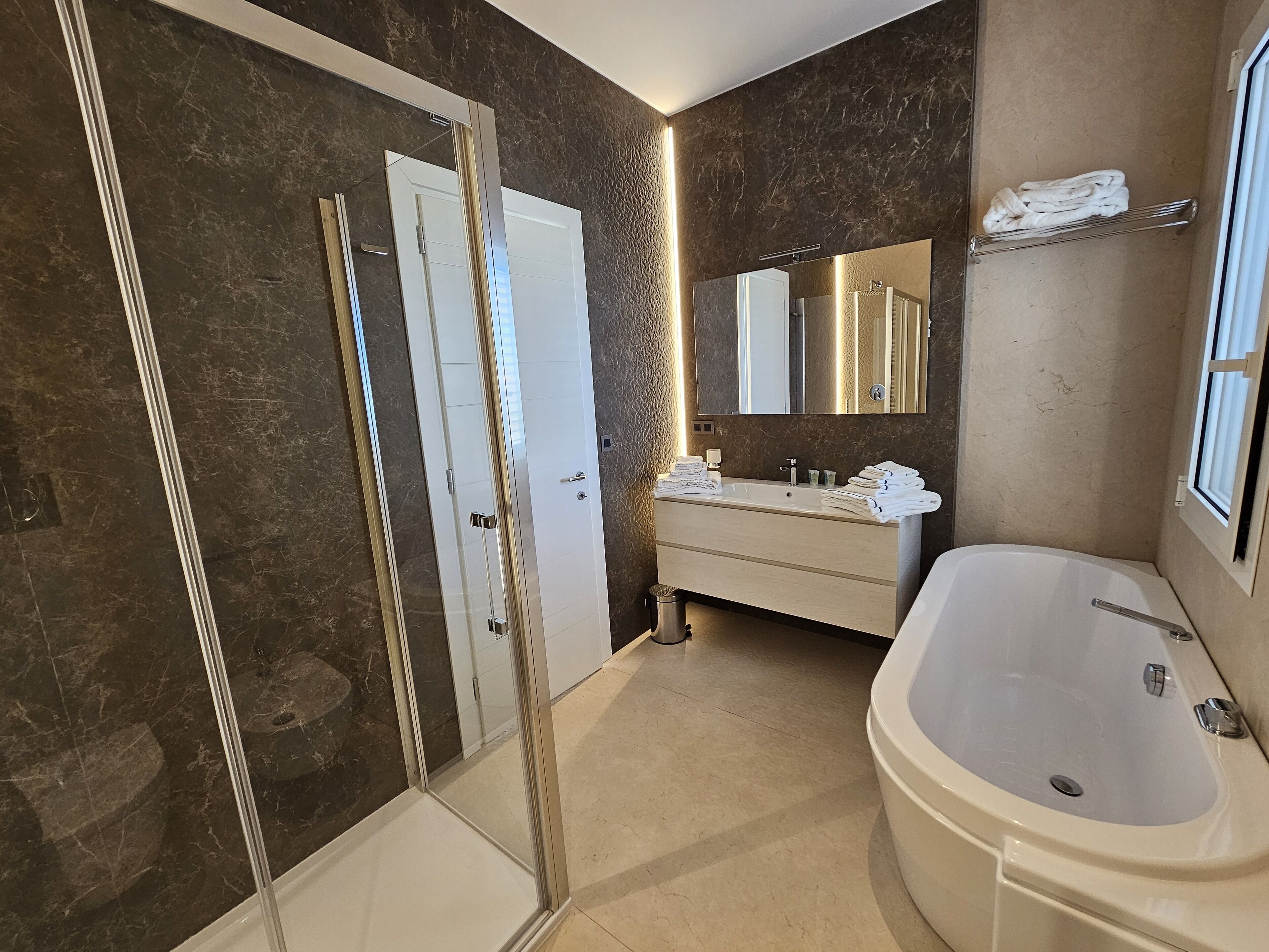 A modern bathroom with a glass-enclosed shower, a large freestanding bathtub, and a vanity with a mirror.