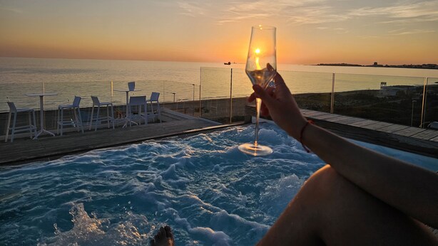Une vue sur le coucher de soleil depuis un espace aménagé près de la piscine, avec des chaises longues et un verre de vin.