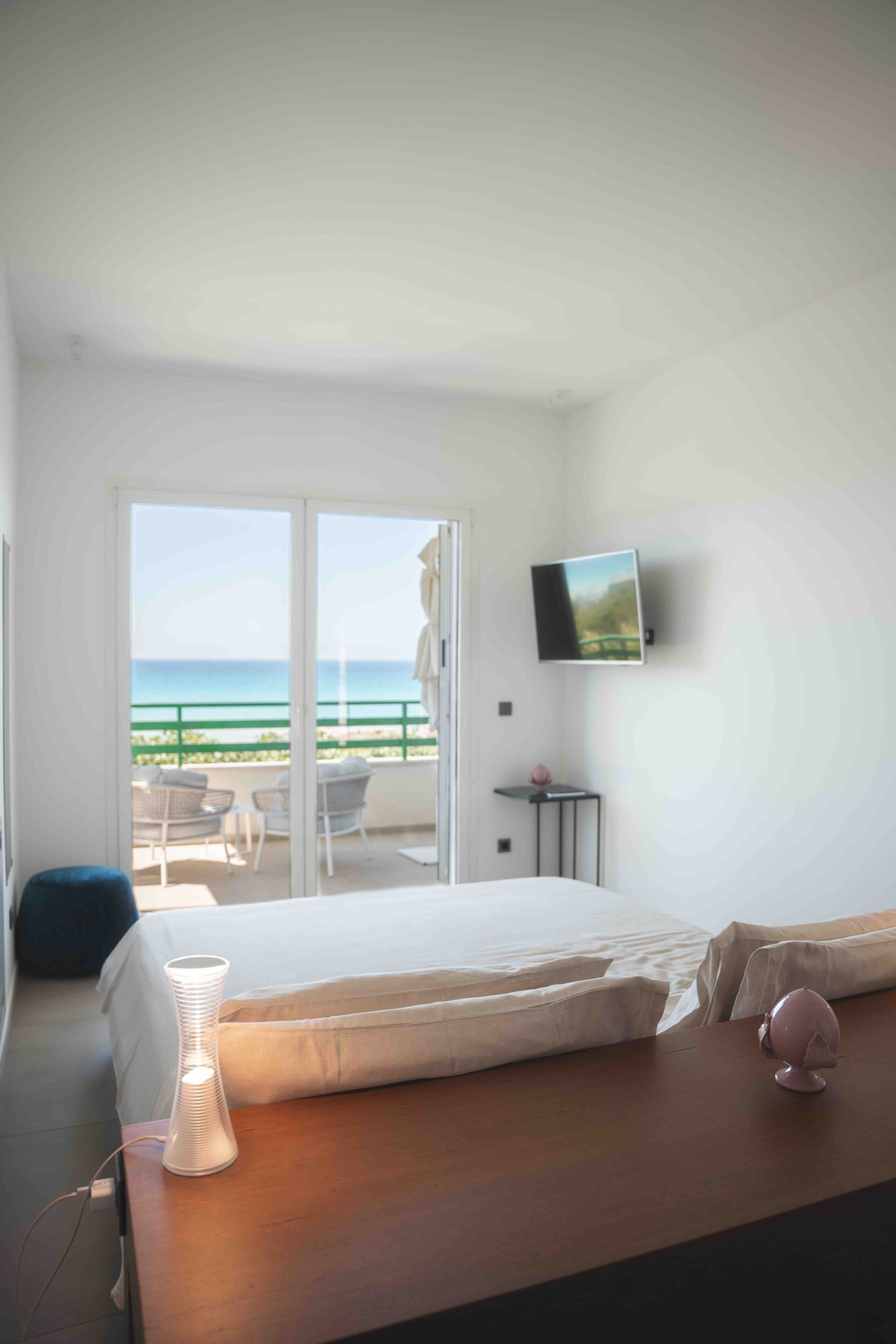 Une chambre d’hôtel avec un lit, une lampe de chevet, une télévision et un balcon donnant sur l’océan.