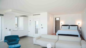 Une chambre d’hôtel moderne, équipée d’un lit, d’un canapé, d’une chaise, d’une petite table et d’une salle de bain visible à travers une porte ouverte.