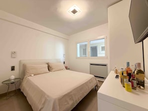 A bedroom with a bed, a small table, a TV, and a window.