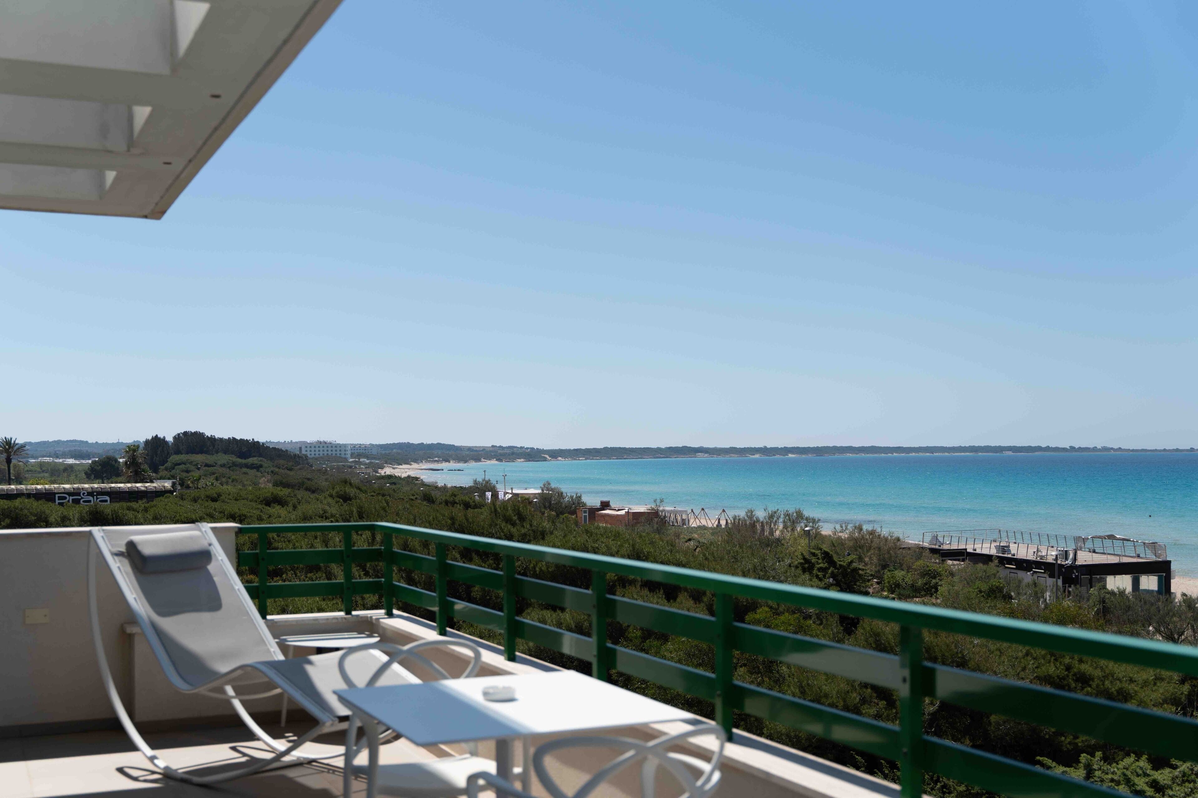 Uma varanda com vista para o mar, uma espreguiçadeira e uma mesa.