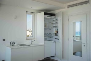 A compact kitchen with a built-in refrigerator, a window, and a door leading to a balcony.