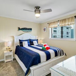 A bedroom with a bed, a nightstand, a ceiling fan, a window with curtains, and a wall-mounted artwork. - Walk to beach - Condo with indoor pool and spa (Hilton Head Island)