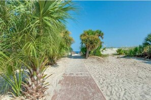 A sandy pathway leading to a beach with palm trees and a clear blue sky. - Walk to beach - Condo with indoor pool and spa (Hilton Head Island)