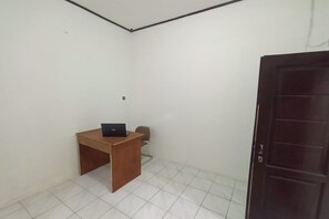 Une petite pièce vide, avec un bureau en bois et un ordinateur portable, une chaise et une porte en bois sombre.