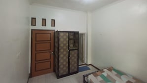 Une petite pièce au mobilier sommaire, avec une porte en bois, une armoire à motifs et un petit lit.